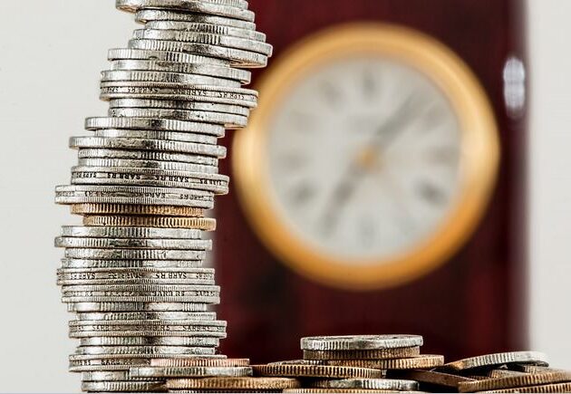 Stack Of Coins In Front Of Clock