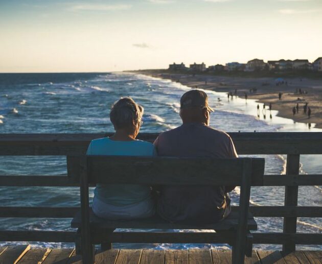 Old Couple Sitting On Bench At Beach